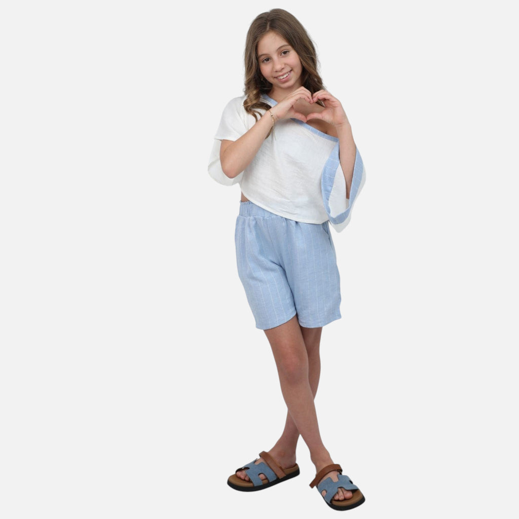 A young girl wearing a Nounami white off-shoulder top with blue trim and light blue pinstripe linen-blend shorts.