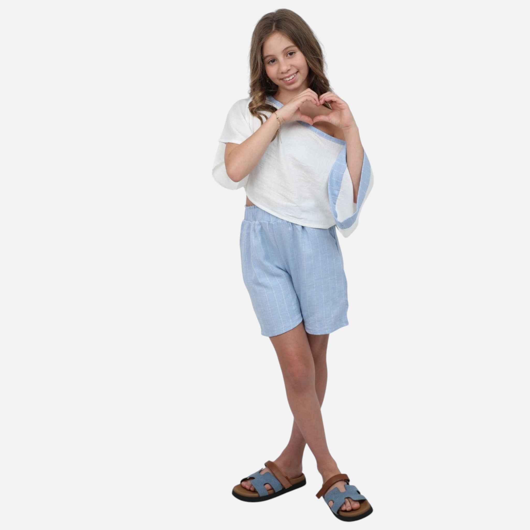A young girl wearing a Nounami white off-shoulder top with blue trim and light blue pinstripe linen-blend shorts.